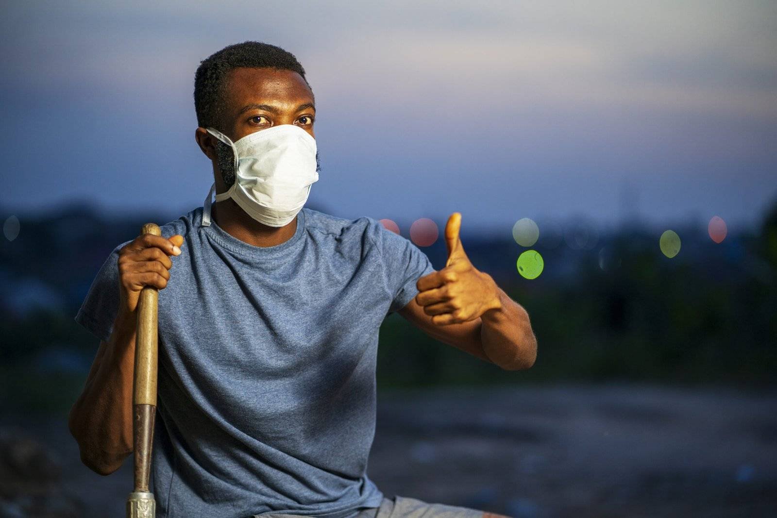 Young African American male in a protective face mask holding a shovel and gesturing thumbs-up sign